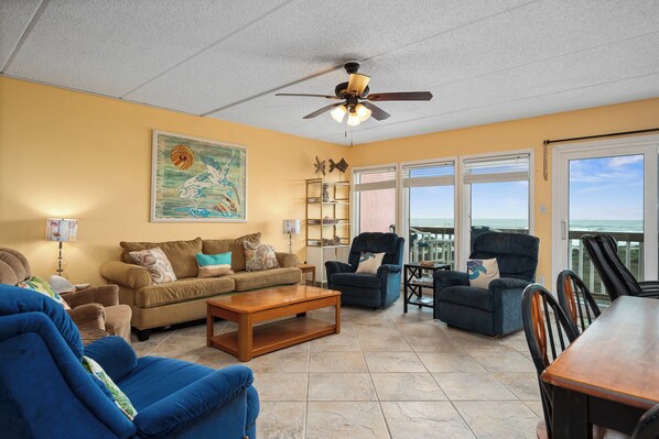 A living room with a ceiling fan, a large painting, a sofa, a coffee table, and a view through the glass doors.