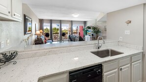 Una cocina moderna con lavavajillas, un fregadero y un comedor visible a través de amplios ventanales.