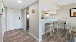 Cocina moderna con armarios blancos, un refrigerador de acero inoxidable y una mesa de comedor de vidrio con taburetes de bar.