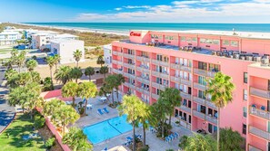 A pink hotel with a pool, surrounded by palm trees and a beach view. - Beachfront Boutique Resort | Sunkissed Retreat | Casa Condo 307 (Port Aransas)
