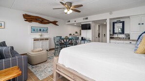 Ein Schlafzimmer mit einem großen Bett, einem Deckenventilator, einem Schreibtisch mit Stühlen, einem Fernseher und einer Küchenzeile.