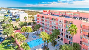 Ein pinkfarbenes Hotel mit Pool, umgeben von Palmen und Blick auf den Strand.