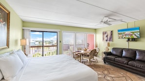 A hotel room with a bed, a dining table with chairs, a leather sofa, a ceiling fan, and a TV. - Beachfront Boutique Resort | Seaside Haven | Casa Condo 406 (Port Aransas)