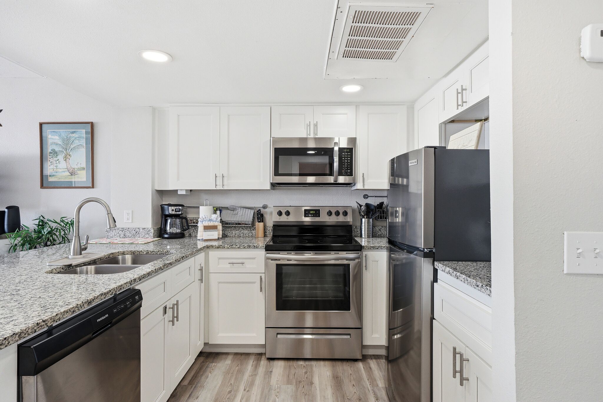 A modern kitchen with white cabinets, stainless steel appliances, a dishwasher, and a granite countertop.