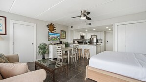 A modern hotel room with a bed, a dining area, kitchenette, and a ceiling fan.