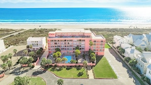 A multi-story hotel with a pool, located near a beach.