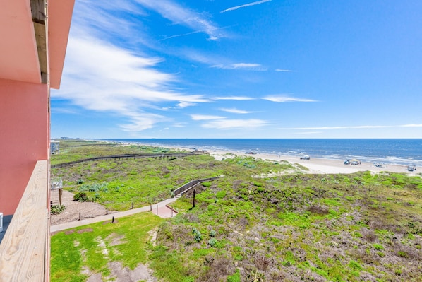 Une vue sur la côte depuis un balcon donnant sur une plage, une promenade en bord de mer et une ville lointaine.