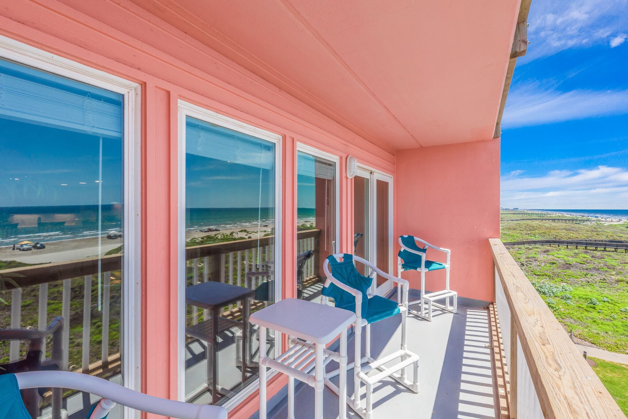 Un balcón con sillas y una mesa blancos, con vista a una playa y al océano.