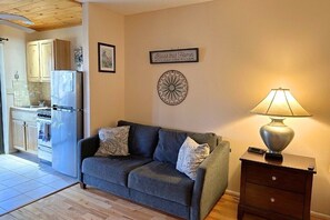 A living room with a sofa, a lamp, a wall decoration, and a kitchen in the background.