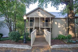 A two-story building with a balcony on the second floor, a covered walkway leading to the entrance, and a tree to the right.