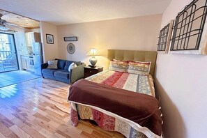 A bedroom with a bed, a nightstand, a lamp, a sofa, and a view of the outside.