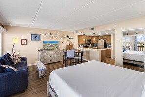 Una habitación de hotel compacta con cama, sofá, escritorio pequeño y kitchenette.