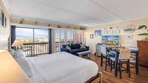 A hotel room with a bed, a desk, a chair, a sofa, and a balcony with a view. - Beachfront Boutique Resort | Pelican's Perch | Casa Condo 506 (Port Aransas)