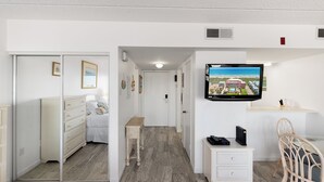 Ein Hotelzimmer mit einem Bett, einem Schminktisch, einem kleinen Tisch, einem an der Wand montierten Fernseher und einem Sessel.