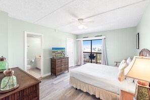 Relax in this serene room with a large bed, wooden dresser, and TV, plus a balcony with a view of the surrounding landscape.
