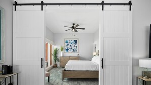 Une chambre à coucher avec un lit, un bureau, un ventilateur de plafond et un tableau accroché au mur.