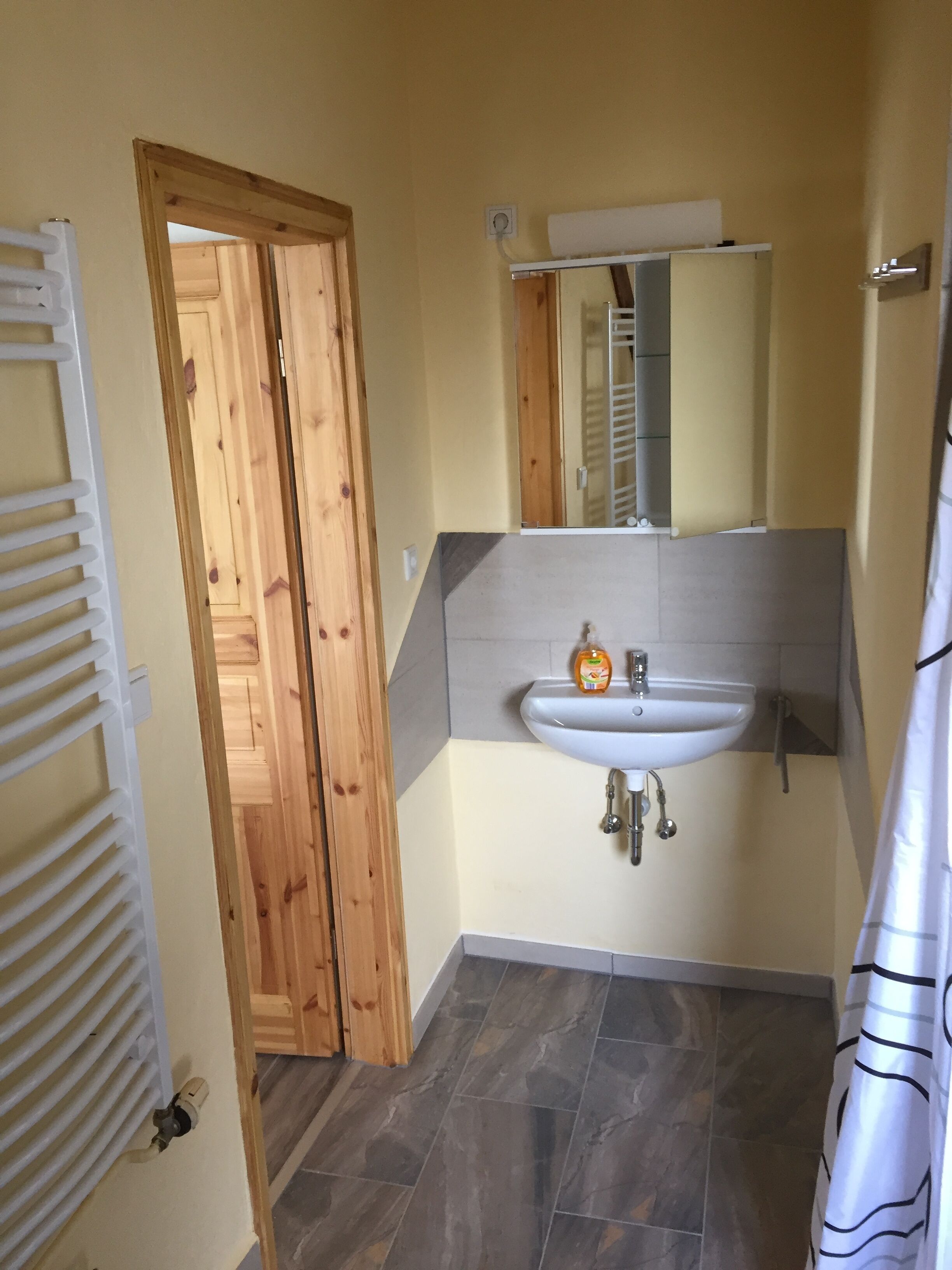 A bathroom with a wooden door, a white sink, a mirror, and a shower curtain.