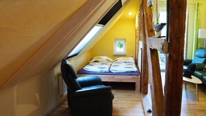 A cozy attic bedroom with a sloped ceiling, a bed with patterned bedding, a black leather chair, and a wooden floor. - Segelwohnung - Meerzauber. Gutshaus Reidervitz - Großer Lindengarten (Altenkirchen)
