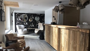Eine moderne Bar mit Holztresen, zwei weißen Stühlen, einem runden Spiegel und einer Deckenleuchte.