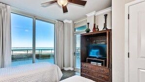 A hotel room with a large bed, a TV, and a balcony with a view of the beach.