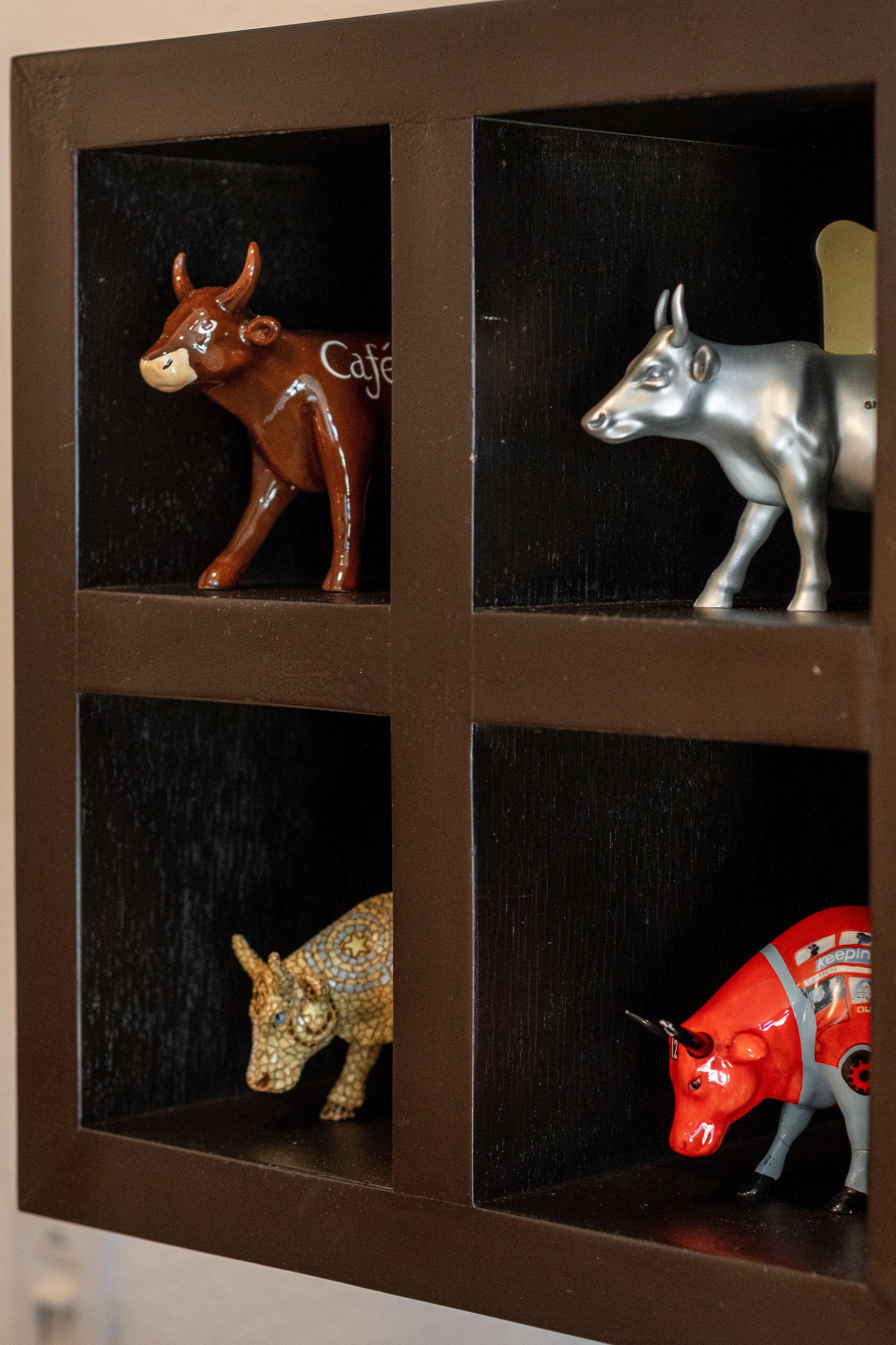 A wooden cabinet with four shelves, each holding a different cow figurine.