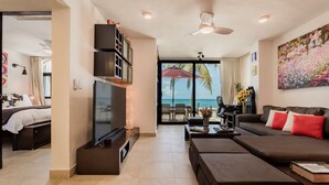 A modern living room with a flat-screen TV, a sofa, a coffee table, and a view of the ocean through large windows. - Depa Bliss Cancún • Beachfront · King Beds · Pool · Luxury Stay • Best Host (Cancún)
