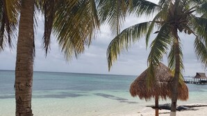 A beach with clear turquoise water, palm trees, and a thatched hut. - Depa Bliss Cancún • Beachfront · King Beds · Pool · Luxury Stay • Best Host (Cancún)