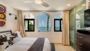 A bedroom with a bed, a ceiling fan, a TV, and windows with a view of the sea. - Depa Bliss Cancún • Beachfront · King Beds · Pool · Luxury Stay • Best Host (Cancún)