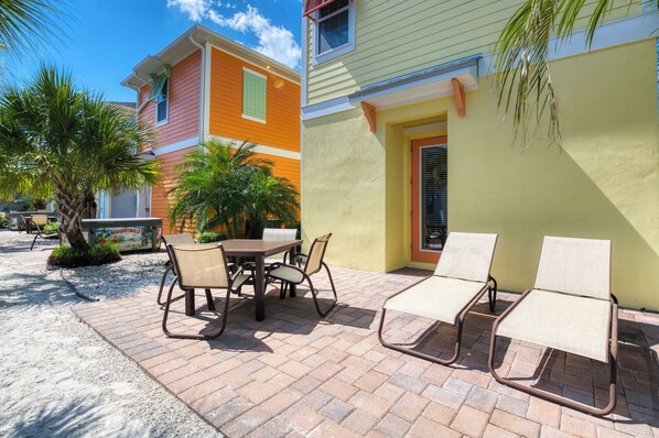 An outdoor patio with a table and chairs, a bench, and a palm tree.