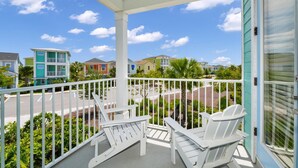 Un balcon avec des fauteuils Adirondack blancs, une balustrade blanche et une vue sur des maisons colorées et des palmiers.