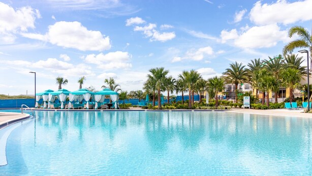 A clear blue pool with lounge chairs and umbrellas, surrounded by palm trees and a clear sky. - Classic Margaritaville Cottage with Pool, Full Kitchen & Outdoor Living (Kissimmee)