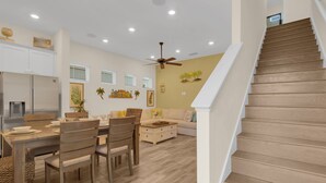 A modern kitchen with white cabinets, a dining table with chairs, and a staircase leading to the upper floor. - Classic Margaritaville Cottage with Pool, Full Kitchen & Outdoor Living (Kissimmee)