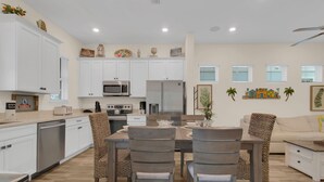 A modern kitchen with white cabinets, a dining area with wooden chairs, and a living room with a sofa and a coffee table. - Classic Margaritaville Cottage with Pool, Full Kitchen & Outdoor Living (Kissimmee)