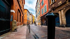 Eine Kopfsteinpflasterstraße gesäumt von historischen Gebäuden, mit einer Mischung aus Backstein- und Natursteinfassaden, und einem markanten schwarzen Poller im Vordergrund.