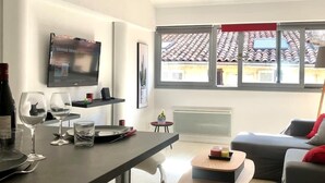 Ein modernes Wohnzimmer mit Essbereich, einem an der Wand befestigten Flachbildfernseher und Blick auf ein Ziegeldach durch große Fenster.