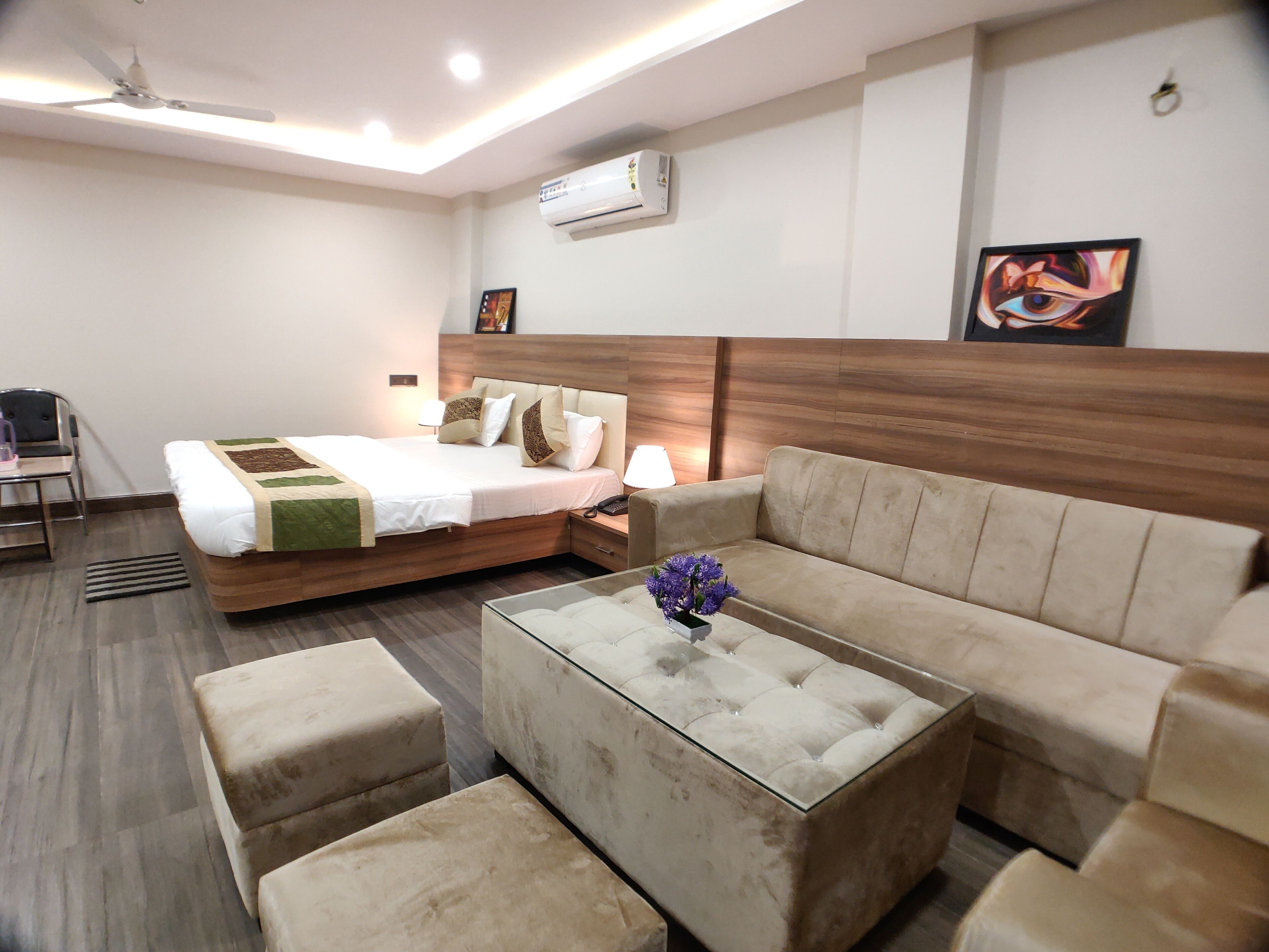 A hotel room with a bed, a sofa, a coffee table, a desk, and an air conditioning unit.