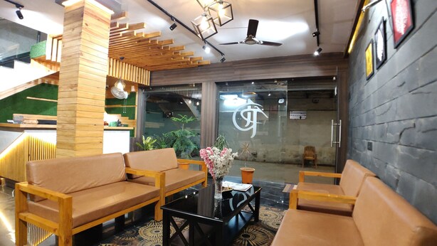 A reception area with wooden furniture, a glass wall with a logo, and a ceiling fan. - Hotel Atul Residency (Satna)