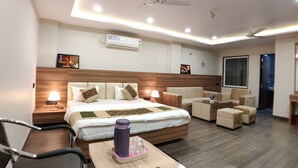 A modern hotel room with a large bed, a desk with a chair, a sofa, and a ceiling fan. - Hotel Atul Residency (Satna)
