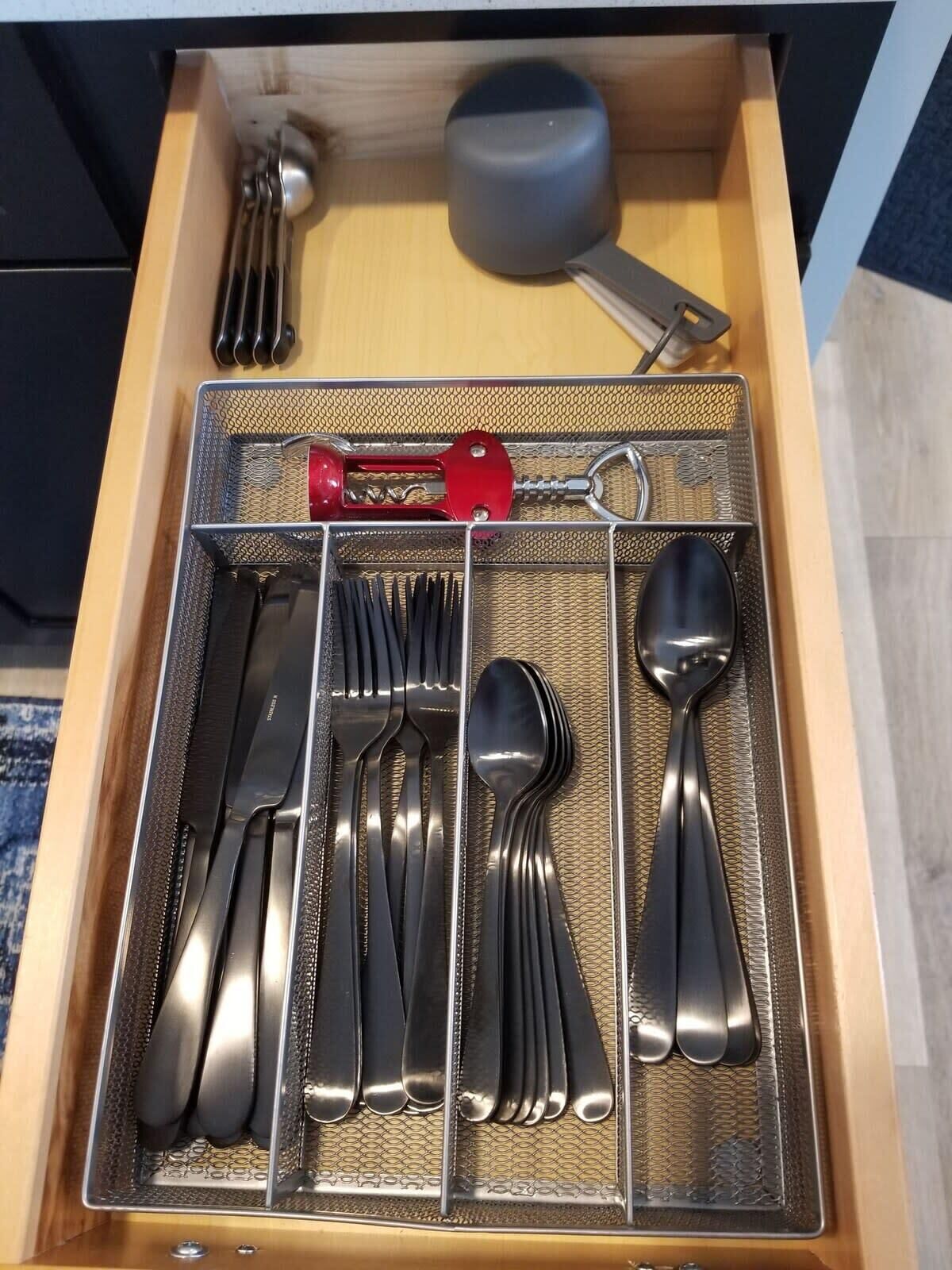 Eine Schublade mit ordentlich angeordnetem Besteck, darunter Gabeln, Messer und Löffel, sowie ein roter Flaschenöffner.