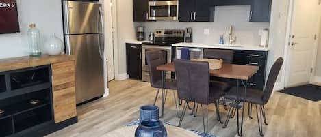 A modern kitchen with dark cabinets, stainless steel appliances, and a dining area with a round table and chairs.