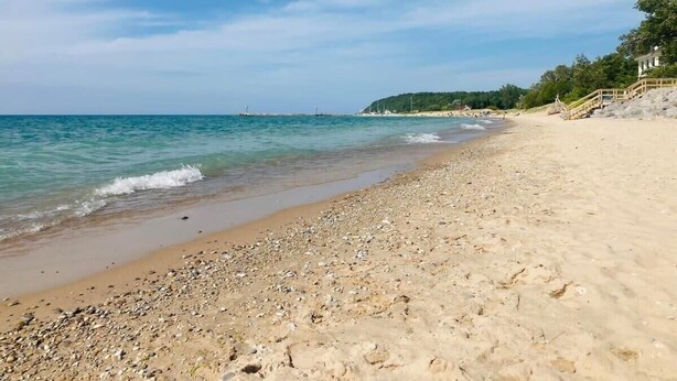 Ein Strand mit Kieselsteinen, einem klaren Himmel und einem Gebäude in der Ferne.