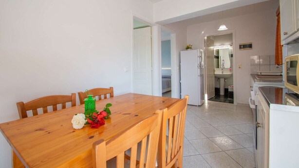 A compact kitchen with a wooden dining table and chairs, a refrigerator, and a sink.