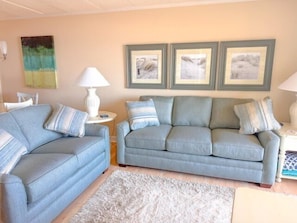 En stue med to sofaer, et hvidt tæppe og billeder i rammer på væggen.