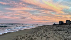 Ein Strand mit Sonnenuntergang, Wellen und Gebäuden im Hintergrund.