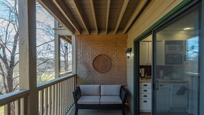 Ein Balkon mit einer Rattan-Couch, einem Holztisch und Blick auf eine Küche durch eine Glastür.