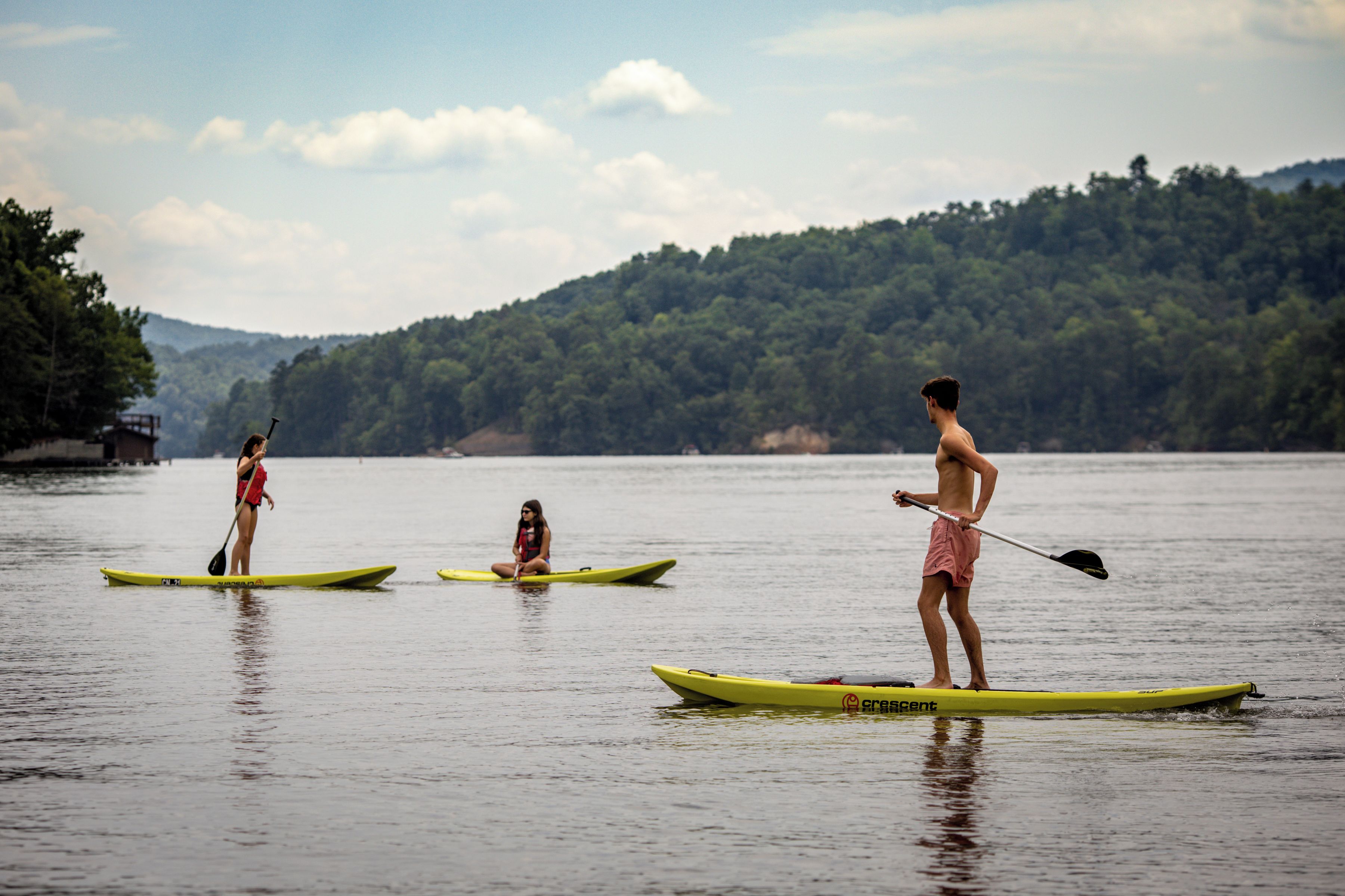 Three individuals on paddleboards in a calm body of water with a forested hillside in the background.