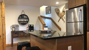 A kitchen with a stainless steel refrigerator, a coffee maker, and a wooden island with stools.