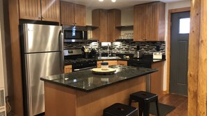 A modern kitchen with wooden cabinets, stainless steel appliances, a black countertop, and a sign indicating Wi-Fi availability.