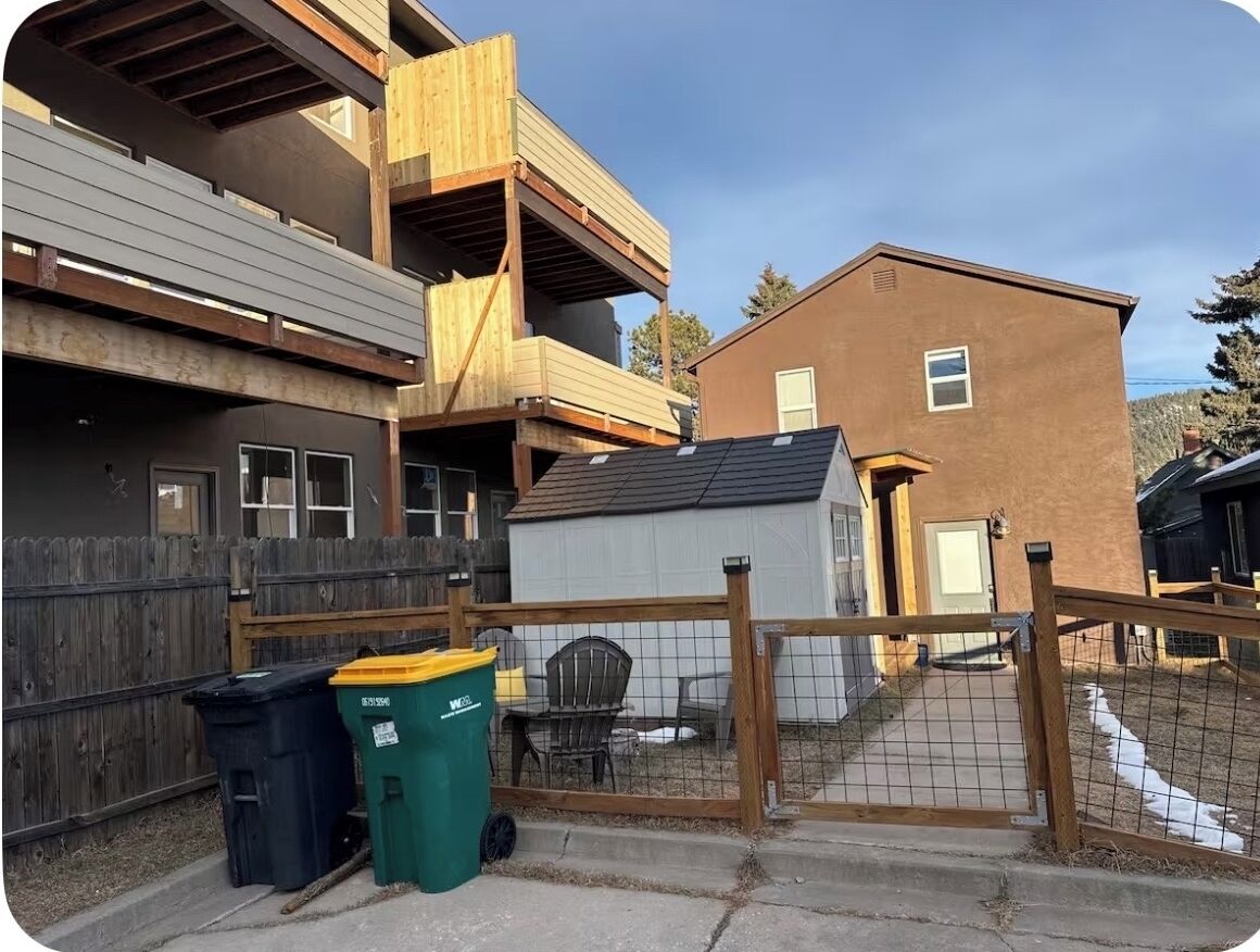 A residential area with a two-story building, a fenced yard, and a small shed.