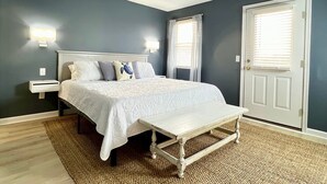 A bedroom with a bed, bedside tables, a ceiling fan, and a door. - Vast Views | Remodeled Townhome, Pool, Pier Access, Lighthouse Views + Pets (Chincoteague Island)